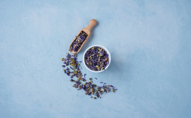 Thé sec à base de plantes aromatiques lavande et camomille en vrac près de tasse blanche sur table en bois bleu