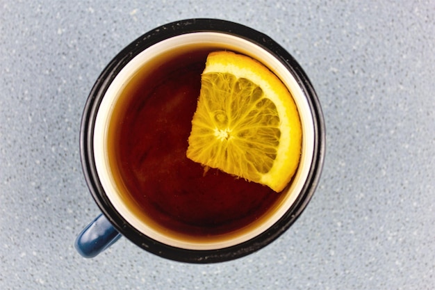 Thé avec une tranche d'orange dans une tasse en métal sur fond bleu Le concept de thé réconfortant aux fruits