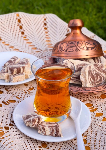 Thé turc dans une coupe en verre et halva en marbre sur une table avec une nappe faite à la main et un fabricant de bonbons