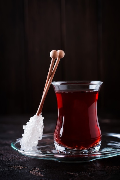 Thé turc dans une tasse en verre traditionnelle avec du sucre caramélisé et de la menthe sur dark