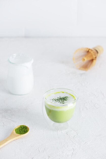 Thé végétalien matcha latte au lait de coco dans un verre sur fond clair.