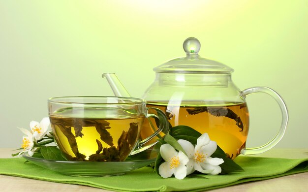 Thé vert au jasmin dans une tasse et une théière sur une table en bois sur fond vert