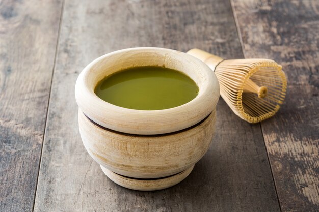 Thé vert Matcha dans un bol et fouet en bambou, sur table en bois