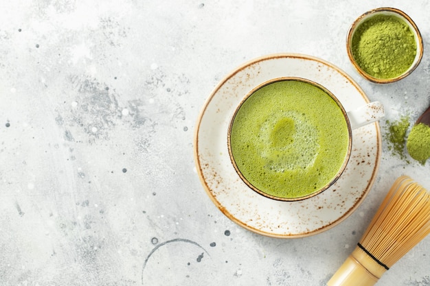 Thé vert matcha latte dans une tasse avec de la crème sur un béton léger