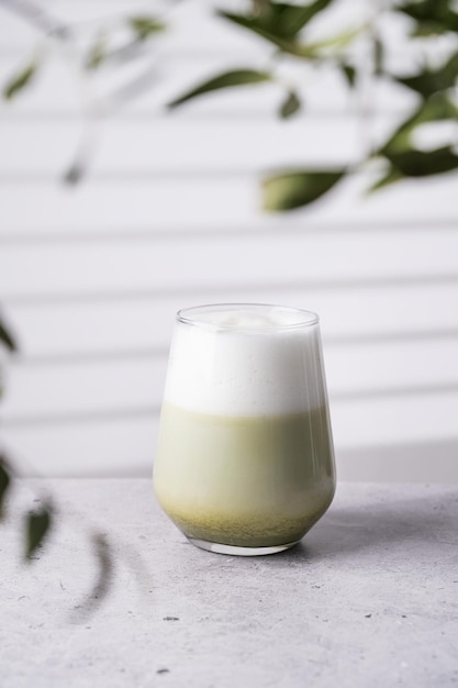 Thé vert matcha latte japonais avec du lait de soja en verre sur fond clair avec des branches et de l'ombre