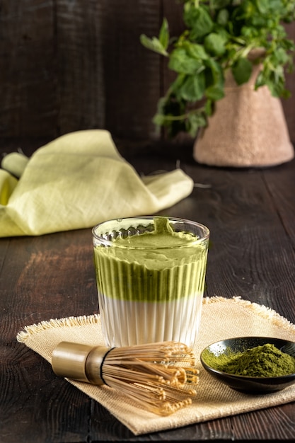 Thé vert matcha latte, poudre de matcha et fouet en bambou sur fond de bois, vertical.