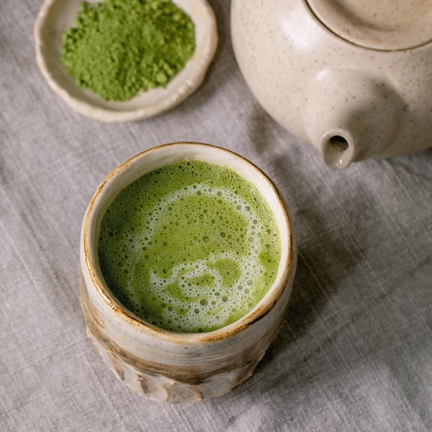 Thé vert mousseux traditionnel japonais matcha latte dans une tasse en céramique faite à la main théière matcha en poudre et fouet en bambou debout sur une nappe en lin gris Boisson saine Image carrée