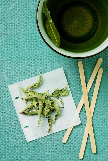 Thé à La Verveine Au Citron Dans Une Tasse Avec Un Sachet De Thé Fait à La Main Sur Un Bureau Vert Marée. Vue De Dessus. Mise à Plat