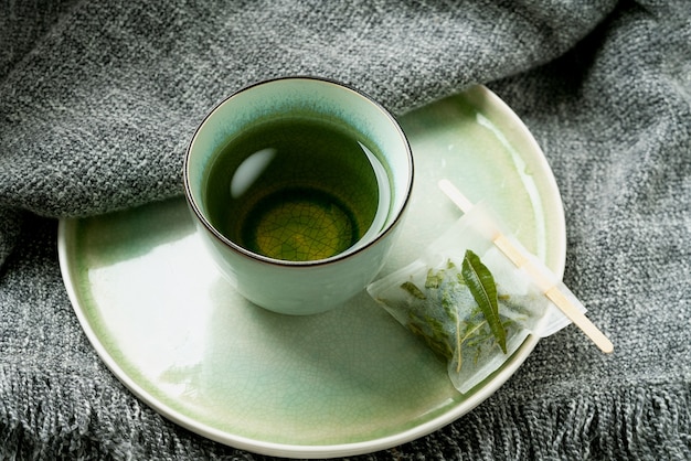 Thé à la verveine au citron dans une tasse avec un sachet de thé fait à la main sur une couverture grise. Concept de confort. Fermer.