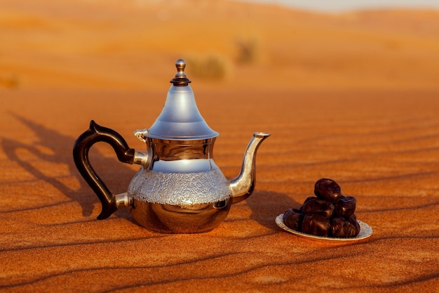 Une théière arabe et des dattes dans le désert lors d'un magnifique coucher de soleil symbolisant le ramadan