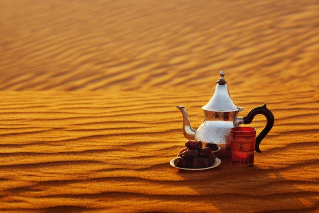 Théière arabe, tasse et dates se tiennent sur le sable dans le désert