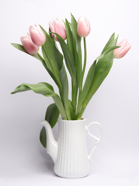 Une théière blanche avec un bouquet de tulipes sur un fond blanc