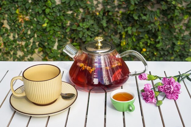 Théière de fleurs avec tasse et fleurs de miel sur une table en bois blanche contre des feuilles vertes