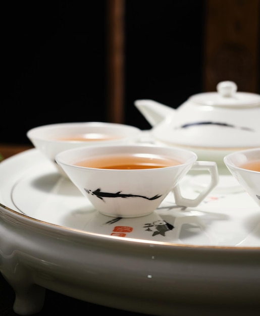 Une théière avec un logo chinois est posée sur une assiette avec une théière et des tasses de thé.