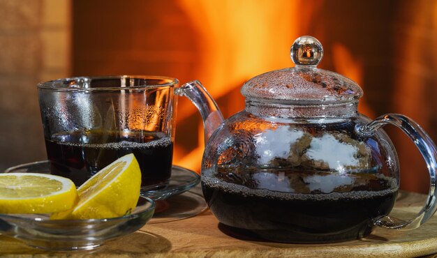 Théière et tasse en verre devant une cheminée confortable dans une maison de campagne.