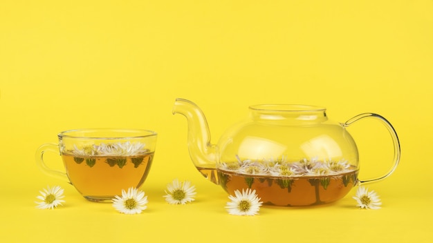 Théière et tasse en verre avec du thé et des fleurs sur fond jaune.