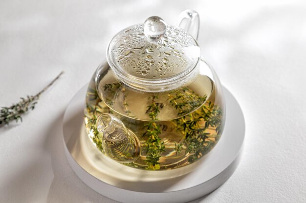 Théière de tisane chaude au thym sur plateau blanc et fond blanc sous les rayons du soleil