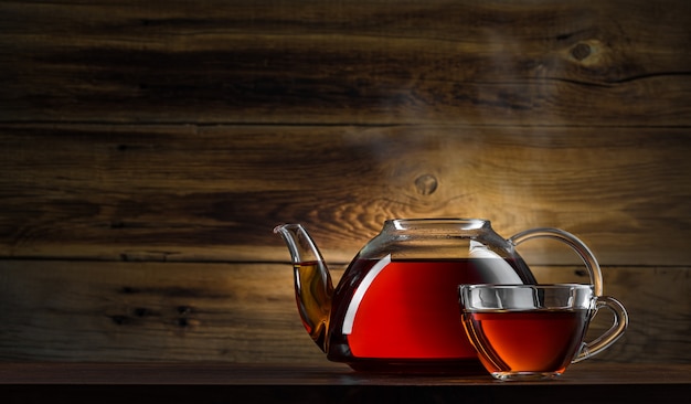 Théière en verre avec du thé noir sur fond de bois