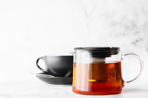 Théière en verre avec une tasse sombre de thé noir isolé sur fond de marbre brillant. Vue aérienne, espace copie. Publicité pour le menu du café. Menu du café. Photo horizontale.