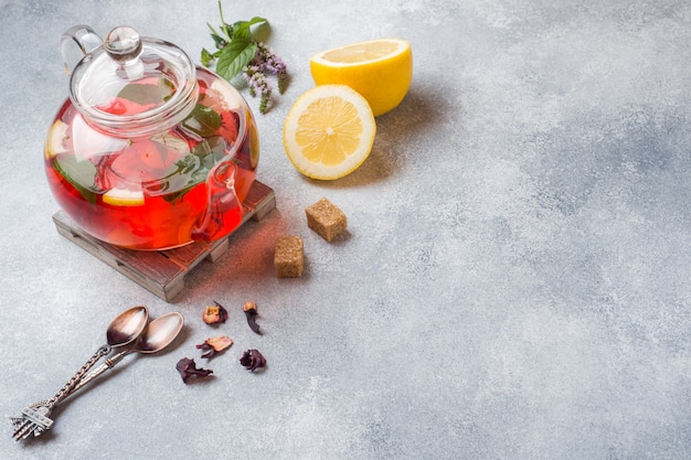 Théière en verre avec thé, menthe et citron sur une table grise avec espace de copie