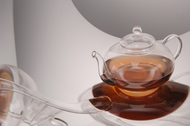 Théière en verre transparent avec du thé sur la surface réfléchissante sur fond gris clair