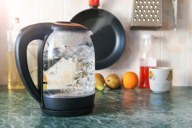 La théière en verre transparent électrique bout dans la cuisine