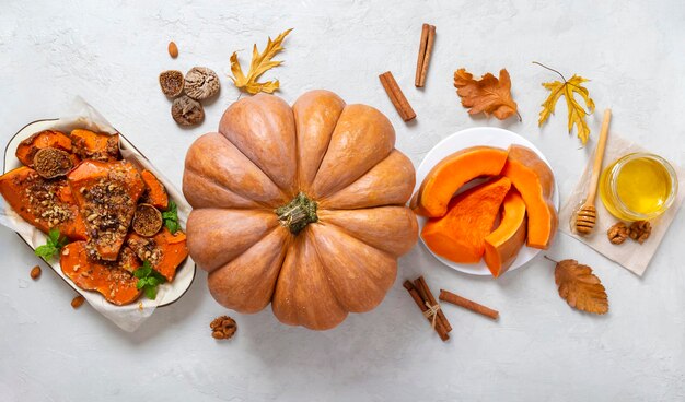 Thème d'automne. Une grande citrouille entière, des plats de citrouille, des feuilles jaunes, du miel sur un fond de béton clair. Baner. Vue de dessus, mise à plat.