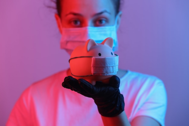 Thème pandémique covid19 Femme en gants tient une tirelire avec masque médical Lumière dégradée néon rouge bleu