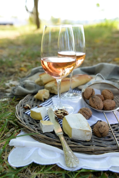 Thème de pique-nique baguette de fromage au vin rose et noix sur un plateau en osier à l'extérieur