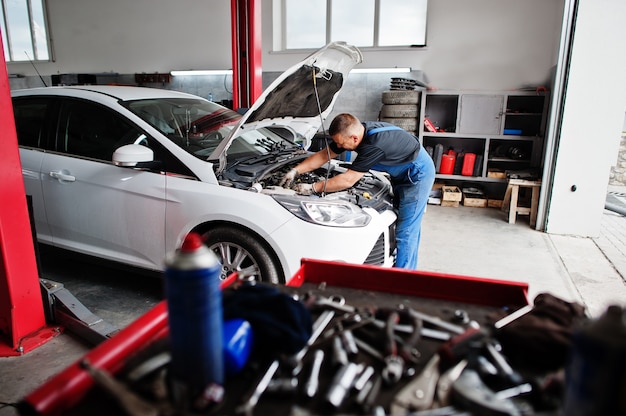 Thème de réparation et d'entretien de voiture. Mécanicien en uniforme travaillant dans le service automobile, vérification du moteur.