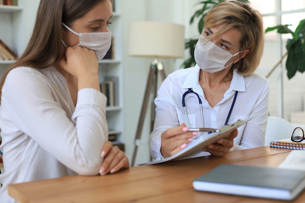 Thérapeute médecin d'âge moyen portant un masque médical en consultation avec le patient au bureau.