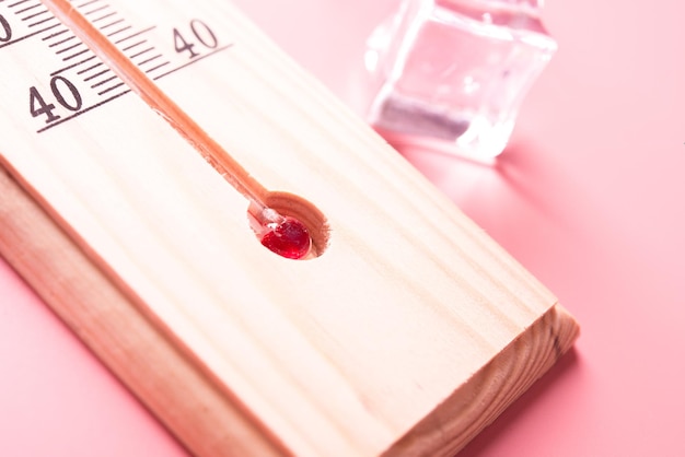 Le thermomètre à bois affiche des températures élevées en Fahrenheit ou Celsius sur fond rose clair avec de la glace