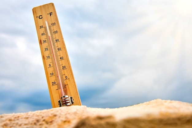 Thermomètre météorologique dans le sable contre le ciel montrant une température ambiante élevée