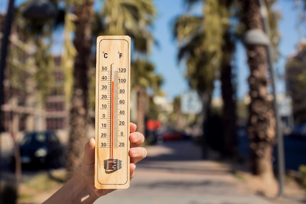 Thermomètre par temps chaud à la main devant la rue avec des arbres et des palmiers pendant la canicule Concept de haute température et de météorologie