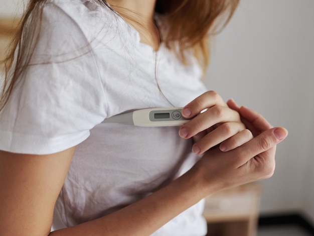 Thermomètre en t-shirt de femme dans les mains vérifiant la température de la santé Photo de haute qualité