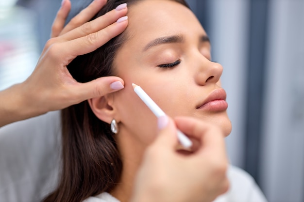 Thread lifting, concept de lifting de la peau, gros plan. Procédure de contour du visage à l'aide de mésothreads, une esthéticienne méconnaissable recadrée prépare le visage du client pour la procédure, contour avec un crayon