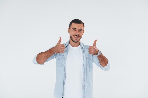 Thumbs up Jeune bel homme debout à l'intérieur sur fond blanc