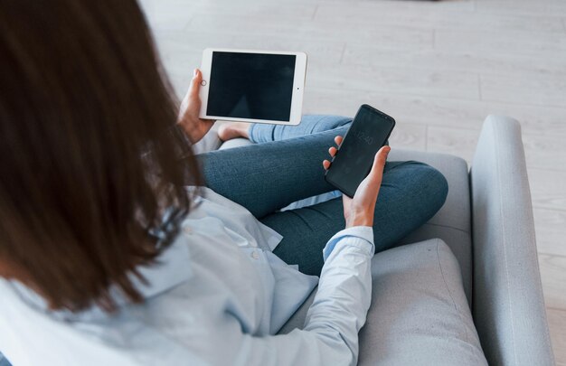 Tient un smartphone et une tablette La jeune femme est à l'intérieur dans la chambre d'une maison moderne pendant la journée