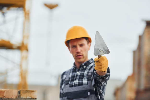 Tient une spatule Un ouvrier du bâtiment en uniforme et équipement de sécurité a un travail sur la construction
