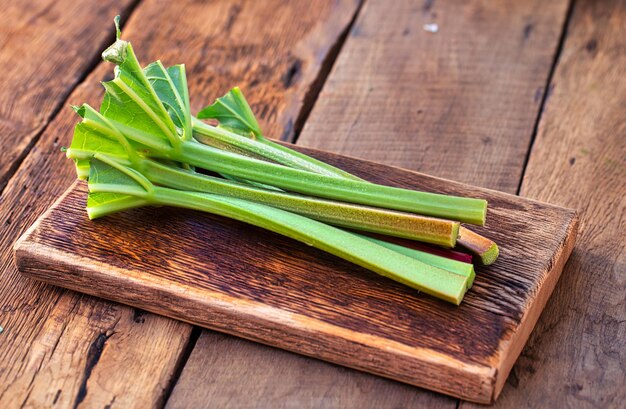 Tiges de rhubarbe fraîches jeunes et juteuses sur une planche de cuisine allongée sur une vieille table en bois