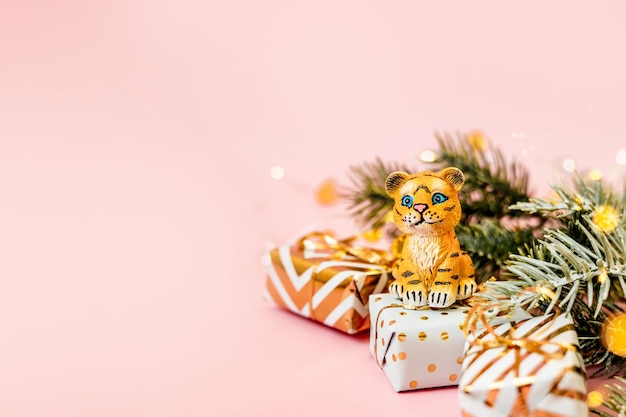 Tigre symbole du nouvel an chinois 2022. Figurine de tigre avec branches d'épicéa et coffrets cadeaux dorés sur fond pastel rose. Espace de copie.