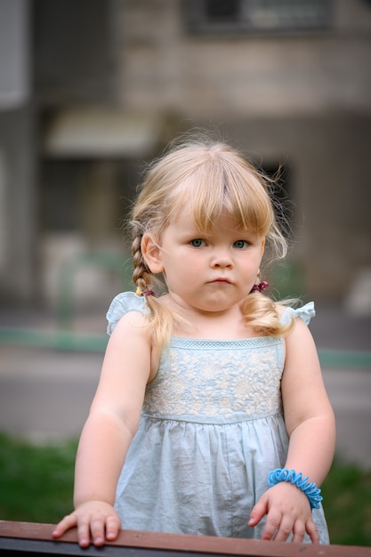 Timide triste petite fille blonde avec deux nattes au fond d'été urbain