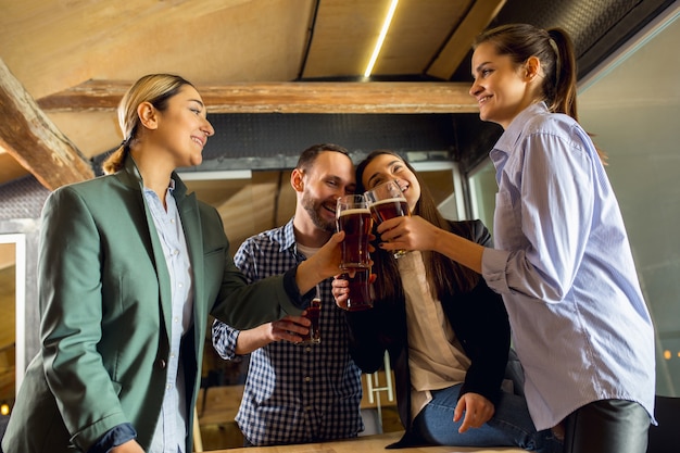 Tintement. Des collègues heureux célébrant un événement d'entreprise après une journée de travail tendue. Ayez l'air ravi, amical, joyeux. Boire de la bière. Concept de culture de bureau, travail d'équipe, amitié, vacances, week-end.