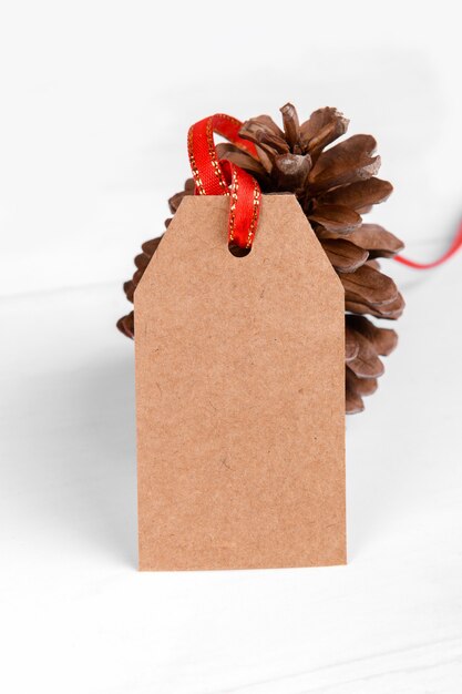 Étiquette de cadeau de Noël de papier craft étiquette présente avec ruban rouge et pomme de pin sur fond blanc.