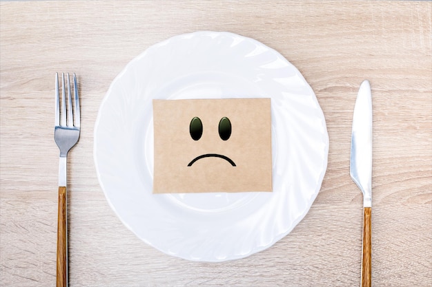 Étiquette avec un smiley triste dans une assiette blanche Nourriture de crise concept affamé