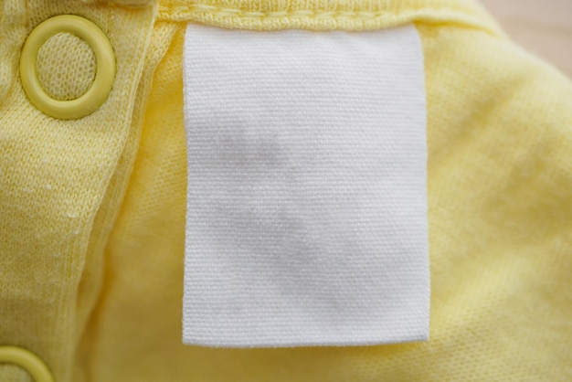 Étiquette de vêtement blanc vierge sur fond de texture de tissu jaune