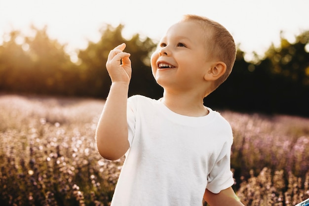 Tir extérieur d'un enfant doux souriant contre le coucher du soleil. Gros plan d'un charmant petit garçon s'amusant dans un champ de fleurs.