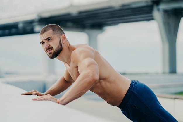 Tir extérieur d'un homme musclé barbu fait pousser des exercices se réchauffe avant l'entraînement