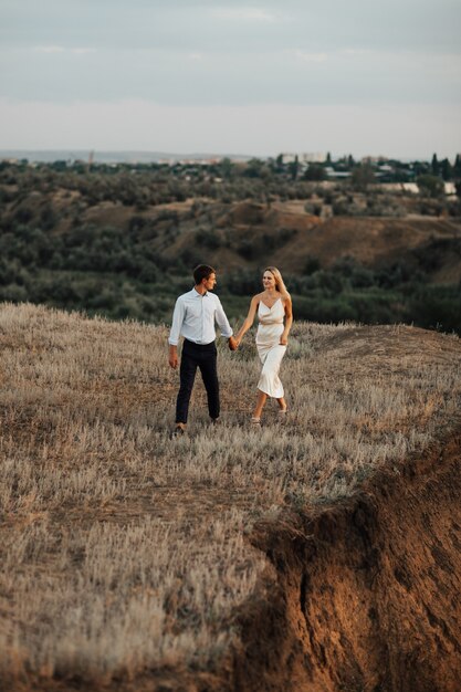 Tir extérieur d'un jeune couple de mariage marchant sur la colline et se tenant la main.