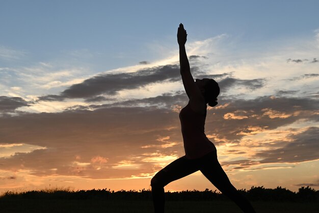 Tir frontal de rétroéclairage d'une jeune femme mince faisant du yoga au coucher du soleil